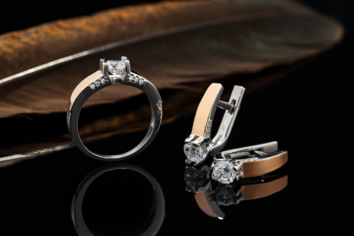 Gold engagement ring and earrings with diamonds on black background with feather behind