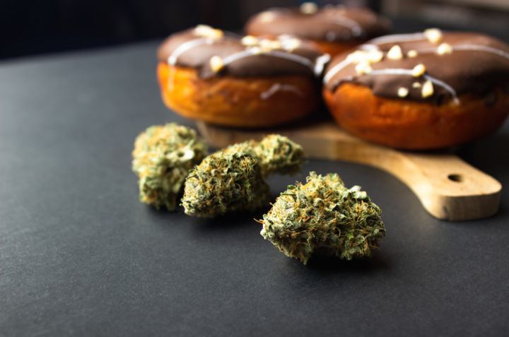 Dry buds of medical marijuana close-up, in the background are donuts covered with chocolate icing, sprinkled with nut crumbs. On a black background