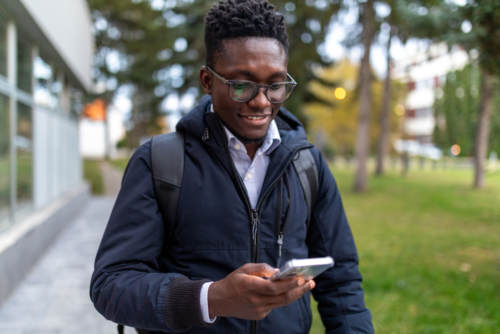 Young man walking outdoors and using his phone
