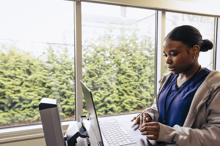 Female nurse working on laptop in medical exam room