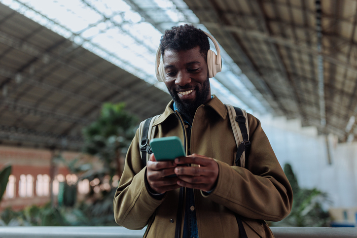 Tourist wearing headphones listening to music and browsing smart phone in airport