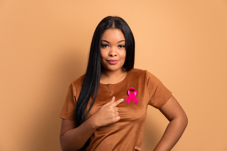 trustworthy african american woman showing pink ribbon in beige colors. breast cancer, awareness concept.