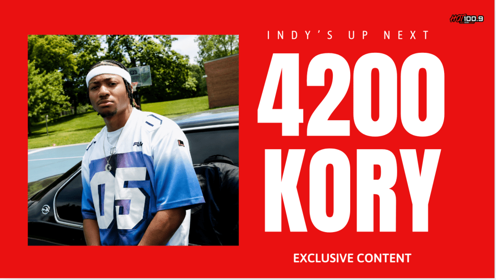 A young man wearing a white and blue jersey with the number 05 standing next to a car. The text overlay reads "INDY'S UP NEXT 4200 KORY EXCLUSIVE CONTENT".