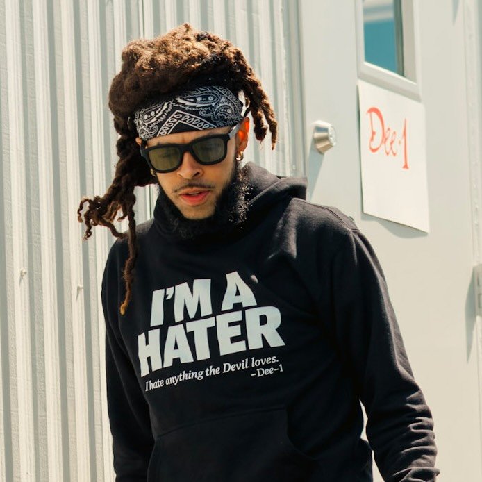 A person wearing sunglasses, a bandana, and a black hoodie with the text "I'M A HATER I hate anything the Devil loves. -Dee-1